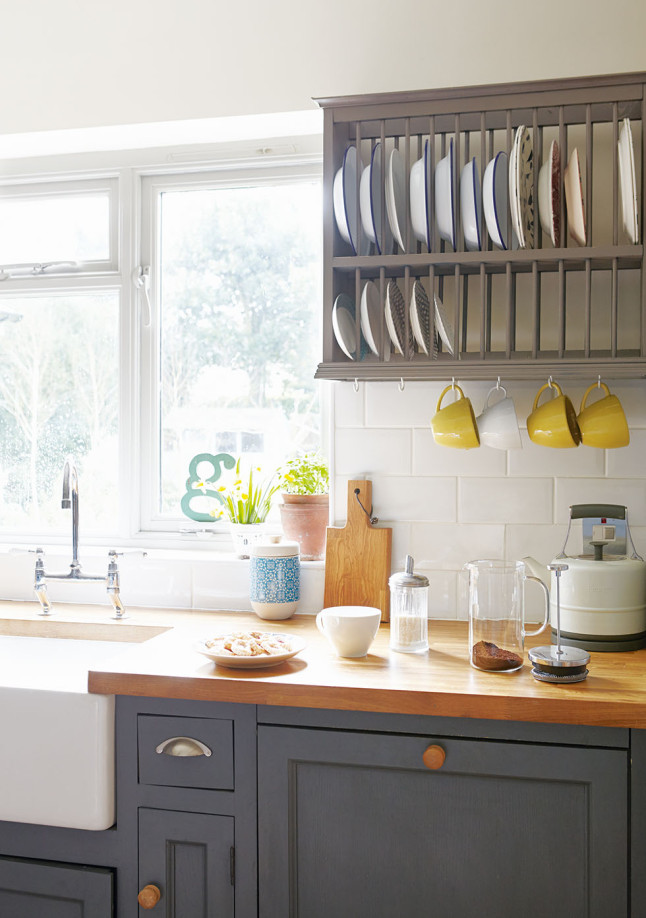 Лакированная деревянная кухонная столешница контрастирует с темным цветом кухонных шкафчиков и сушилкой для тарелок.